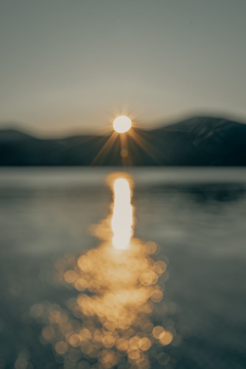 An out-of-focus photo of a sun setting behind mountains, with water reflecting the sun's rays