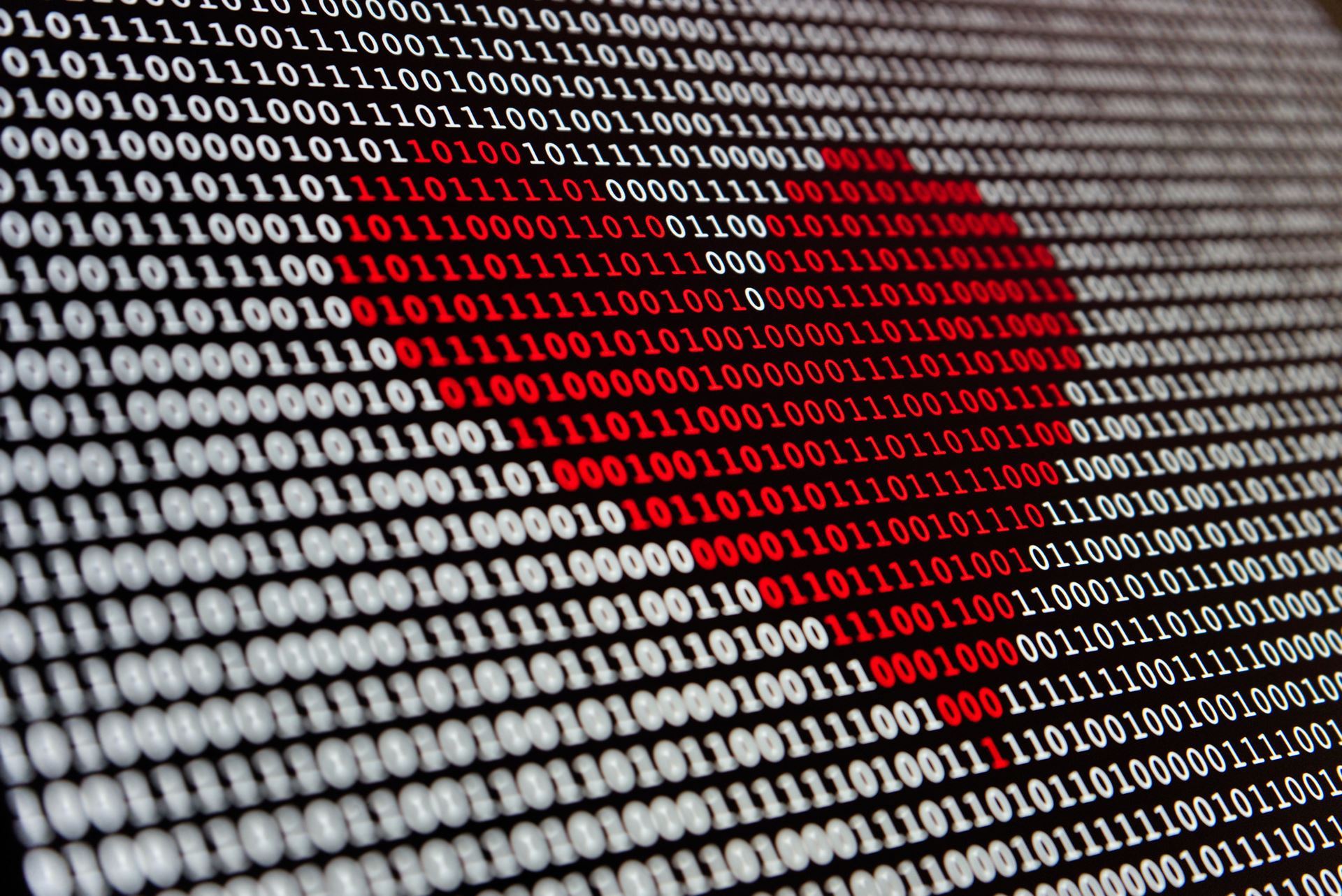 A screen with white binary 0s and 1s against a black background. In the centre, some of the binary numbers are in red font that forms a heart shape.