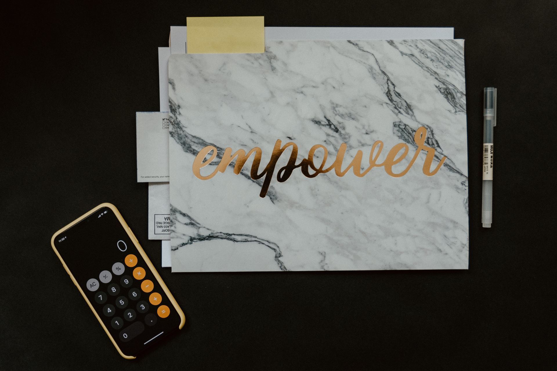 A piece of paper with a stylish marbled background and the word "empower" written on it, a pen, and a smartphone with the calculator app open.